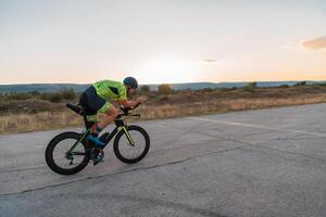Triathlete riding his bicycle during sunset, preparing for a marathon. The warm colors of the sky provide a beautiful backdrop for his determined and focused effort. photo