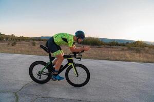 Triathlete riding his bicycle during sunset, preparing for a marathon. The warm colors of the sky provide a beautiful backdrop for his determined and focused effort. photo