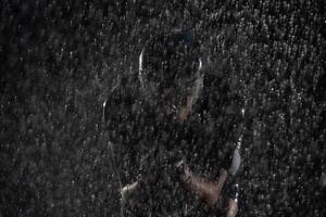 A triathlete braving the rain as he cycles through the night, preparing himself for the upcoming marathon. The blurred raindrops in the foreground and the dark, moody atmosphere in the background add photo