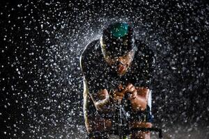 A triathlete braving the rain as he cycles through the night, preparing himself for the upcoming marathon. The blurred raindrops in the foreground and the dark, moody atmosphere in the background add photo