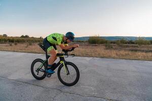 Triathlete riding his bicycle during sunset, preparing for a marathon. The warm colors of the sky provide a beautiful backdrop for his determined and focused effort. photo