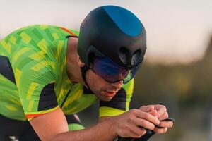 Close up photo of triathlete riding his bicycle during sunset, preparing for a marathon. The warm colors of the sky provide a beautiful backdrop for his determined and focused effort.