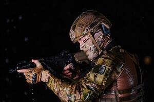 Army soldier in Combat Uniforms with an assault rifle, plate carrier and combat helmet going on a dangerous mission on a rainy night. photo