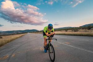 Triathlete riding his bicycle during sunset, preparing for a marathon. The warm colors of the sky provide a beautiful backdrop for his determined and focused effort. photo