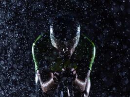A triathlete braving the rain as he cycles through the night, preparing himself for the upcoming marathon. The blurred raindrops in the foreground and the dark, moody atmosphere in the background add photo