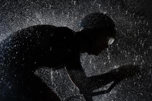 A triathlete braving the rain as he cycles through the night, preparing himself for the upcoming marathon. The blurred raindrops in the foreground and the dark, moody atmosphere in the background add photo