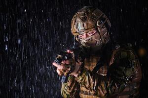 Army soldier in Combat Uniforms with an assault rifle, plate carrier and combat helmet going on a dangerous mission on a rainy night. photo