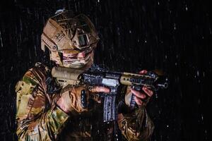 Army soldier in Combat Uniforms with an assault rifle, plate carrier and combat helmet going on a dangerous mission on a rainy night. photo