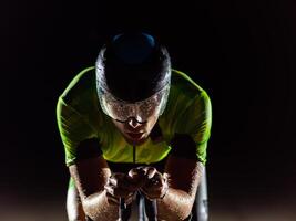 A triathlete rides his bike in the darkness of night, pushing himself to prepare for a marathon. The contrast between the darkness and the light of his bike creates a sense of drama and highlights the photo