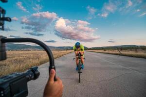 A videographer recording a triathlete riding his bike preparing for an upcoming marathon.Athlete's physical endurance and the dedication required to succeed in the sport. photo