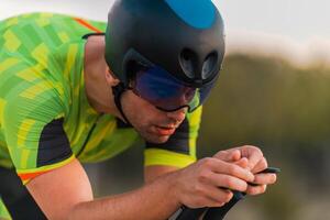Close up photo of triathlete riding his bicycle during sunset, preparing for a marathon. The warm colors of the sky provide a beautiful backdrop for his determined and focused effort.