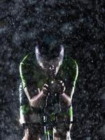 A triathlete braving the rain as he cycles through the night, preparing himself for the upcoming marathon. The blurred raindrops in the foreground and the dark, moody atmosphere in the background add photo