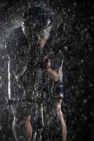 A triathlete braving the rain as he cycles through the night, preparing himself for the upcoming marathon. The blurred raindrops in the foreground and the dark, moody atmosphere in the background add photo