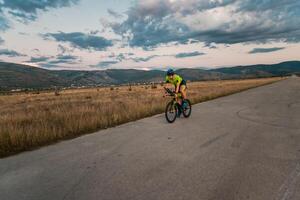 Triathlete riding his bicycle during sunset, preparing for a marathon. The warm colors of the sky provide a beautiful backdrop for his determined and focused effort. photo