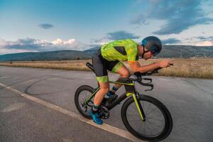 Triathlete riding his bicycle during sunset, preparing for a marathon. The warm colors of the sky provide a beautiful backdrop for his determined and focused effort. photo