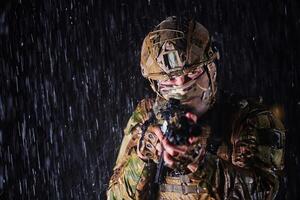 Army soldier in Combat Uniforms with an assault rifle, plate carrier and combat helmet going on a dangerous mission on a rainy night. photo