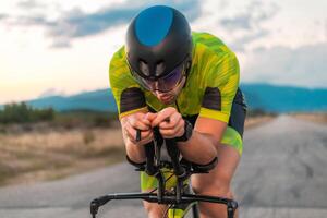 Close up photo of triathlete riding his bicycle during sunset, preparing for a marathon. The warm colors of the sky provide a beautiful backdrop for his determined and focused effort.