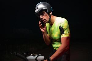 A triathlete using a smartphone while taking a break from a hard night's cycling training photo