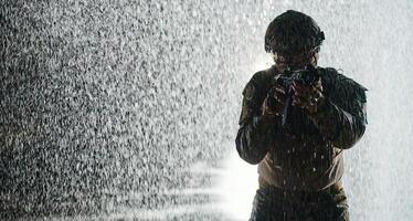 Army soldier in Combat Uniforms with an assault rifle, plate carrier and combat helmet going on a dangerous mission on a rainy night. photo