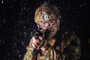 Army soldier in Combat Uniforms with an assault rifle, plate carrier and combat helmet going on a dangerous mission on a rainy night. photo