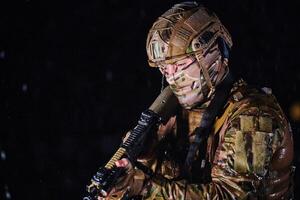 Army soldier in Combat Uniforms with an assault rifle, plate carrier and combat helmet going on a dangerous mission on a rainy night. photo