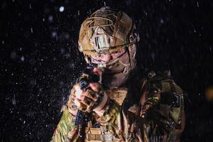 Army soldier in Combat Uniforms with an assault rifle, plate carrier and combat helmet going on a dangerous mission on a rainy night. photo