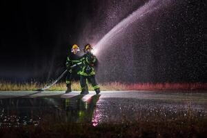 Firefighters using a water hose to eliminate a fire hazard. Team of female and male firemen in dangerous rescue mission. photo