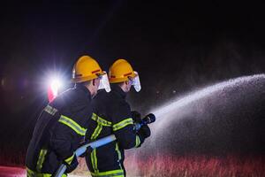 Firefighters using a water hose to eliminate a fire hazard. Team of female and male firemen in dangerous rescue mission. photo