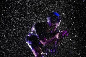 A triathlete braving the rain as he cycles through the night, preparing himself for the upcoming marathon. The blurred raindrops in the foreground and the dark, moody atmosphere in the background add photo