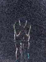 A triathlete braving the rain as he cycles through the night, preparing himself for the upcoming marathon. The blurred raindrops in the foreground and the dark, moody atmosphere in the background add photo