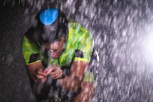 A triathlete braving the rain as he cycles through the night, preparing himself for the upcoming marathon. The blurred raindrops in the foreground and the dark, moody atmosphere in the background add photo