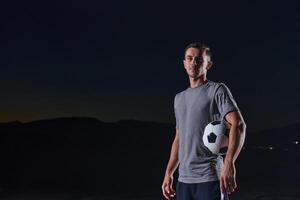 Portrait of a young handsome soccer player man on a street playing with a football ball. photo