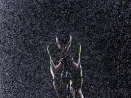 A triathlete braving the rain as he cycles through the night, preparing himself for the upcoming marathon. The blurred raindrops in the foreground and the dark, moody atmosphere in the background add photo