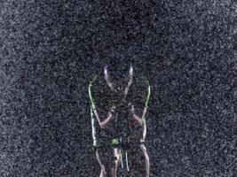 A triathlete braving the rain as he cycles through the night, preparing himself for the upcoming marathon. The blurred raindrops in the foreground and the dark, moody atmosphere in the background add photo