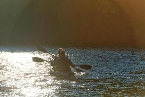A young couple enjoying an idyllic kayak ride in the middle of a beautiful river surrounded by forest greenery in sunset time photo