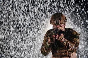 Army soldier in Combat Uniforms with an assault rifle, plate carrier and combat helmet going on a dangerous mission on a rainy night. photo