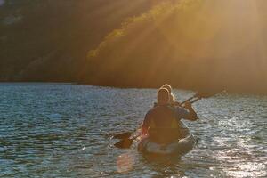 A young couple enjoying an idyllic kayak ride in the middle of a beautiful river surrounded by forest greenery in sunset time photo