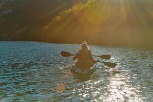 A young couple enjoying an idyllic kayak ride in the middle of a beautiful river surrounded by forest greenery in sunset time photo