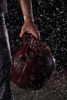 Close up of American Football Athlete Warrior Standing on a Field focus on his Helmet and Ready to Play. Player Preparing to Run, Attack and Score Touchdown. Rainy Night with Dramatic lens flare photo