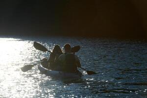 A young couple enjoying an idyllic kayak ride in the middle of a beautiful river surrounded by forest greenery in sunset time photo