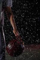 Close up of American Football Athlete Warrior Standing on a Field focus on his Helmet and Ready to Play. Player Preparing to Run, Attack and Score Touchdown. Rainy Night with Dramatic lens flare photo