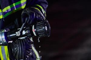 Firefighter using a water hose to eliminate a fire hazard. Team of firemen in the dangerous rescue mission. photo