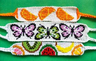 Three white woven DIY friendship bracelets handmade of embroidery bright thread with knots. Alpha weaving with fruit and butterflies patterns photo