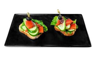 sandwiches with a slice of tender smoked salmon and vegetables on a black plate on a white background top view photo
