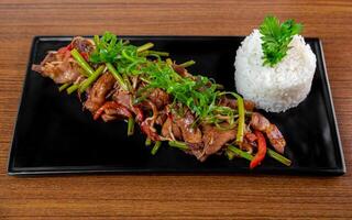 Fried pork with garlic arrows and vegetables with rice on a black plate on wooden table photo