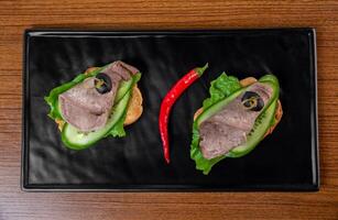 sandwiches with a slice of tender beef and vegetables on a black plate on a wooden table top view photo