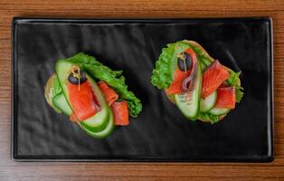 sandwiches with a slice of tender smoked salmon and vegetables on a black plate on a wooden table photo