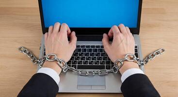 A person in a suit is chained to a laptop photo