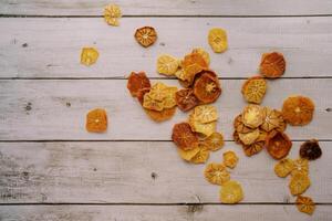 Fruit chips are distributed in the corner of a light wooden background photo
