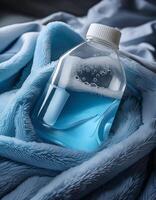 Liquid in a Clear Bottle Rests on a Soft Blue Blanket, Highlighting Its Vibrant Color and Surface Bubbles photo
